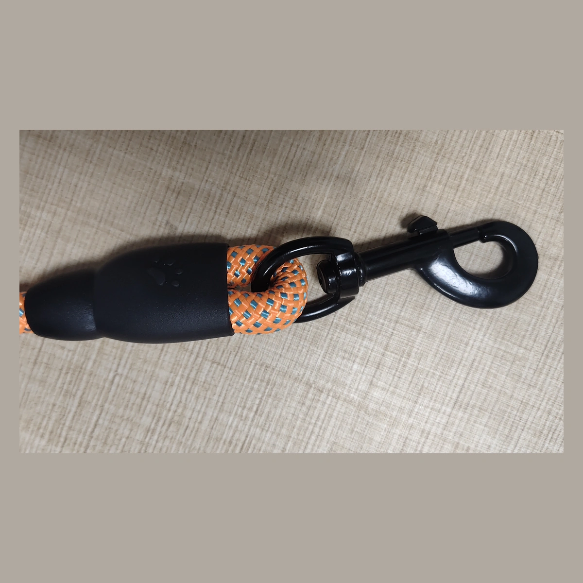 Black metal snap hook and covered rope connection on an orange braided dog leash